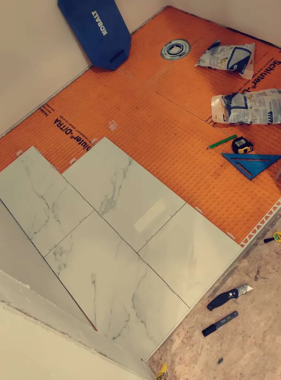 Bathroom floor preparation and tile installation around the drain with waterproof membrane visible